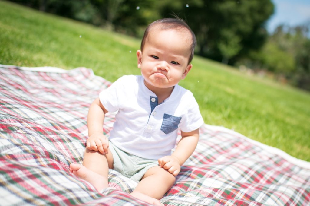 grumpy face toddler sitting on plaid blanket taken during daytime