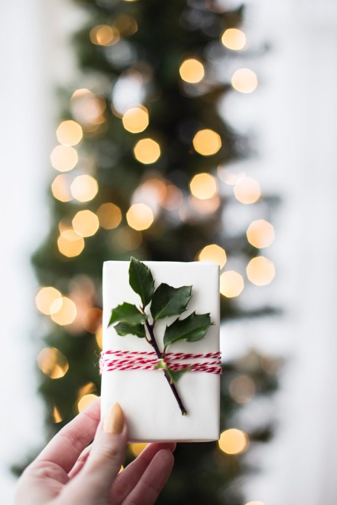 gift card wrapped in white paper, tied with red string and decorated with a sprig of holly.  Use gift cards to budget for the holidays