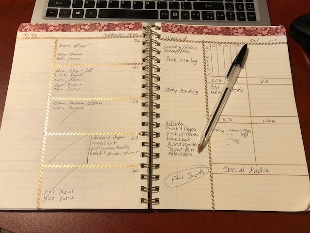 Planner with weekly spread open leaning on laptop keyboard and has an inkpen laying on the page